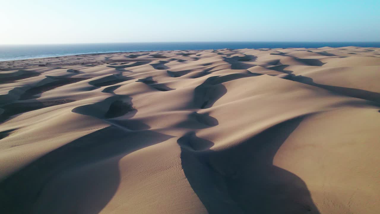 Golden sand dunes roll toward the ocean in this dramatic 4K aerial drone footage of Maspalomas, Gran Canaria, revealing a person trekking across the breathtaking Canary Islands landscape.