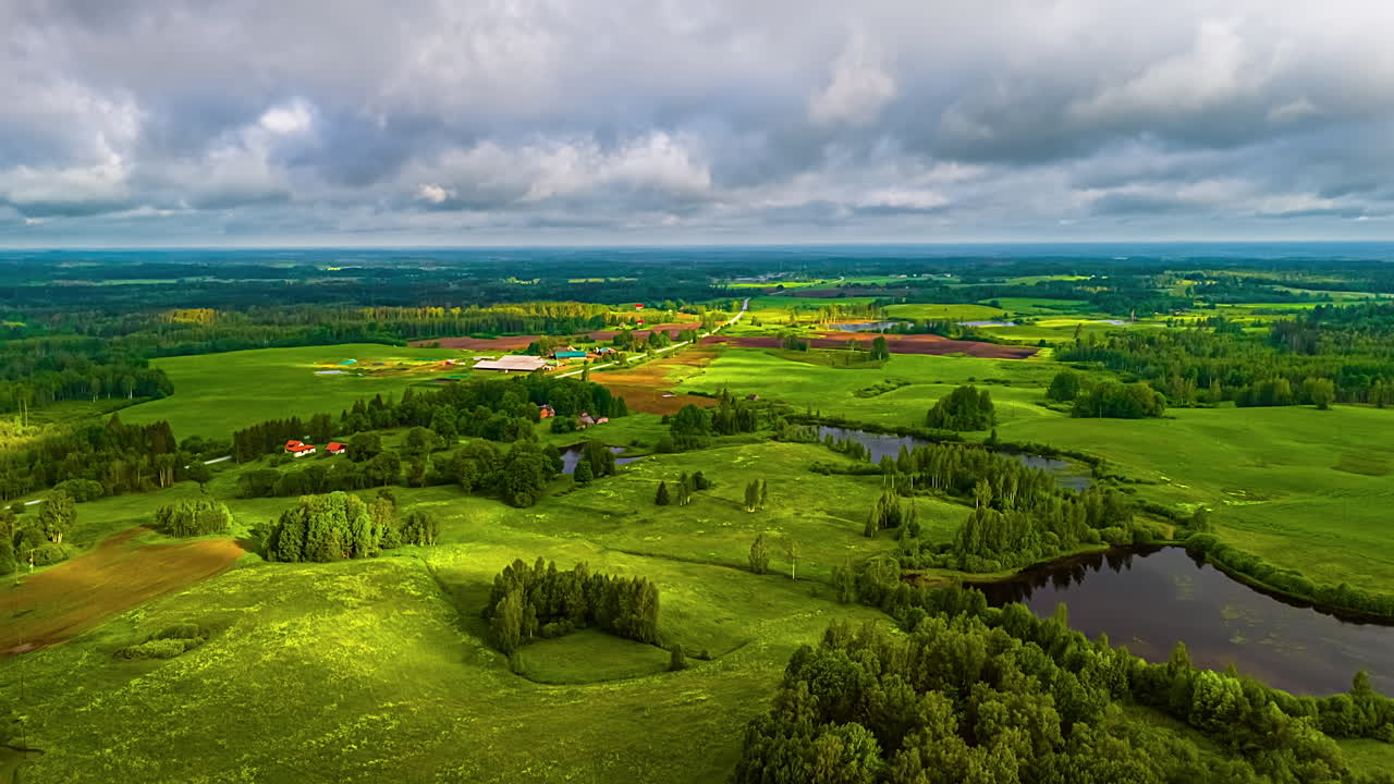 A picturesque time-lapse aerial view of clouds drifting over Latvia’s vibrant green fields, forests, and shimmering lakes in summer