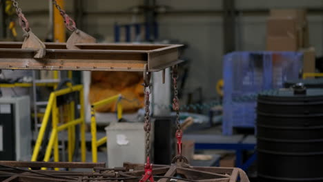 cadenas y polipastos levantando una estructura de moldeo de acero grande y pesada dentro de una nave industrial, parte de una cadena de suministro en el proceso de fabricación de objetos plásticos aleatorios.