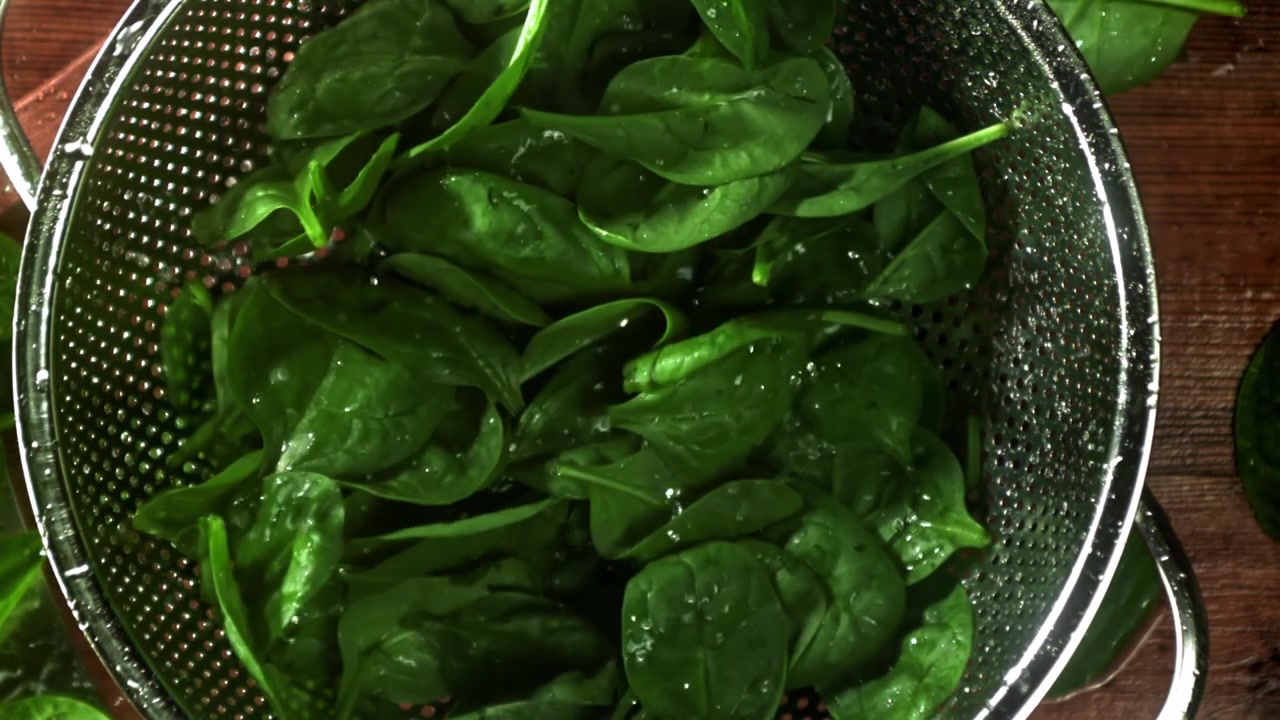 Foglie di spinaci freschi e verdi che cadono in uno scolapasta