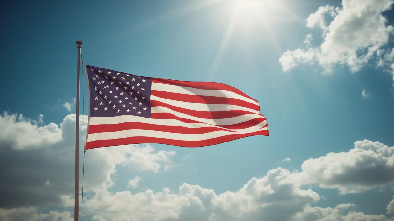 Breeze lifting American flag on pole against vivid blue sky under bright sun, with cumulus clouds