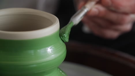 painting a green ceramic pot on a pottery wheel