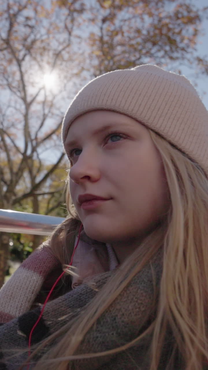 Eftertænksom ung kvinde med hue og tørklæde i efterårssolskin.