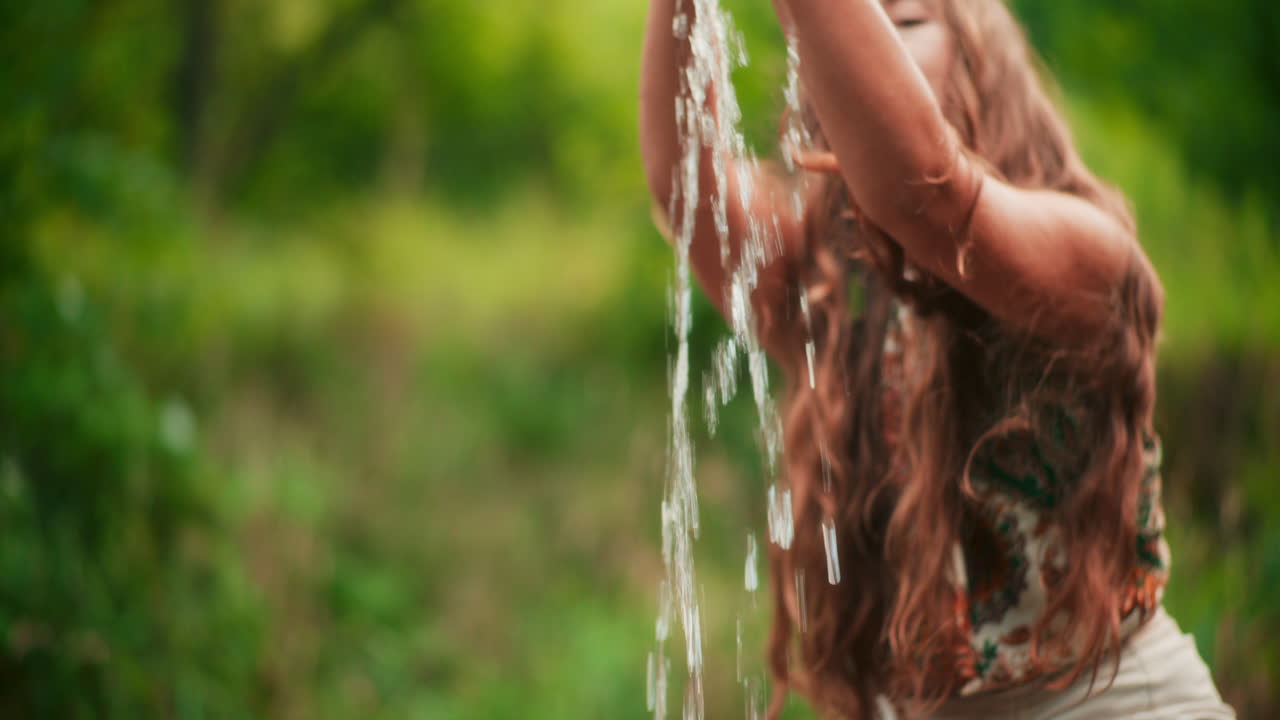 una mujer toma agua de un río en sus manos y se la derrama sobre sí misma