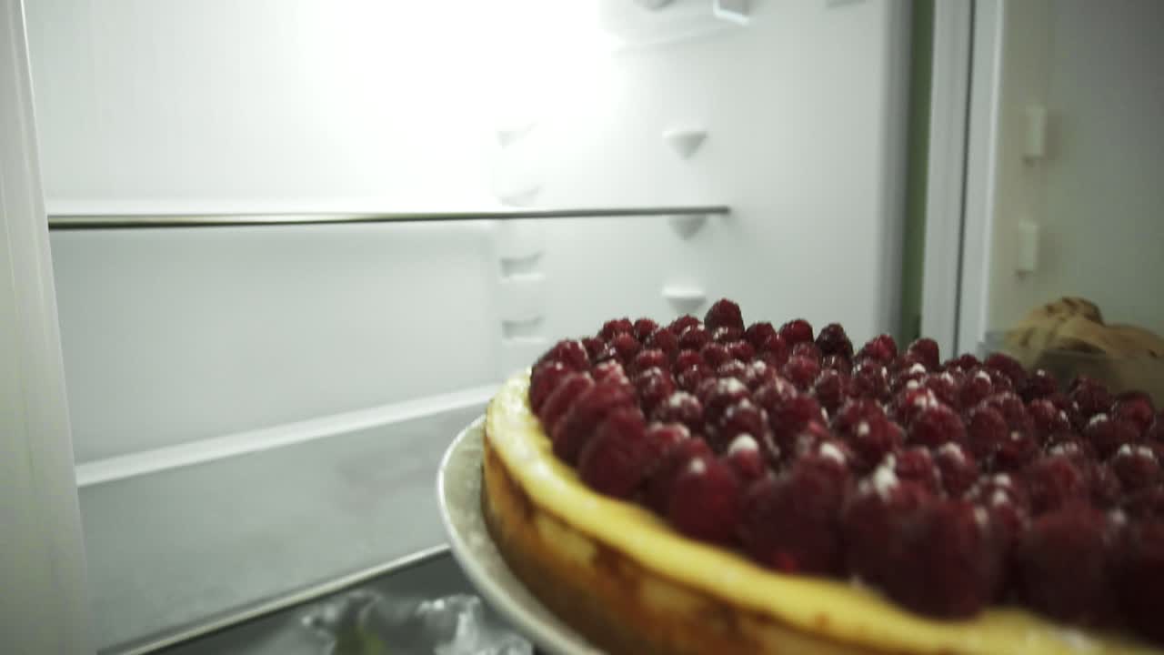 Close Up view of woman's hands holding the plate with the cake decorated with raspberries, opens the fridge and puts in the cake