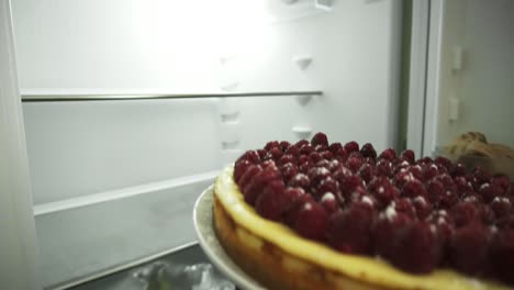 Close-Up-view-of-woman's-hands-holding-the-plate-with-the-cake-decorated-with-raspberries,-opens-the-fridge-and-puts-in-the-cake
