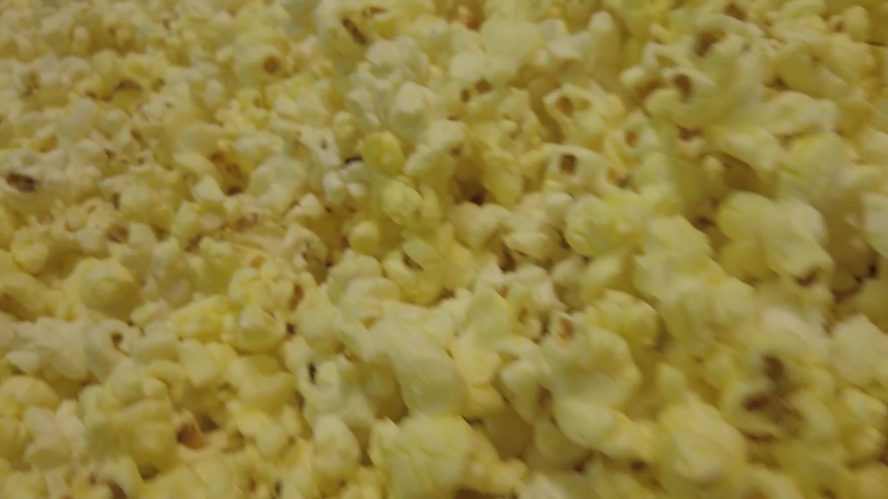 Ripresa al rallentatore di una vasca che si riempie fino all'orlo con popcorn appena scoppiati che traboccano dalla macchina.