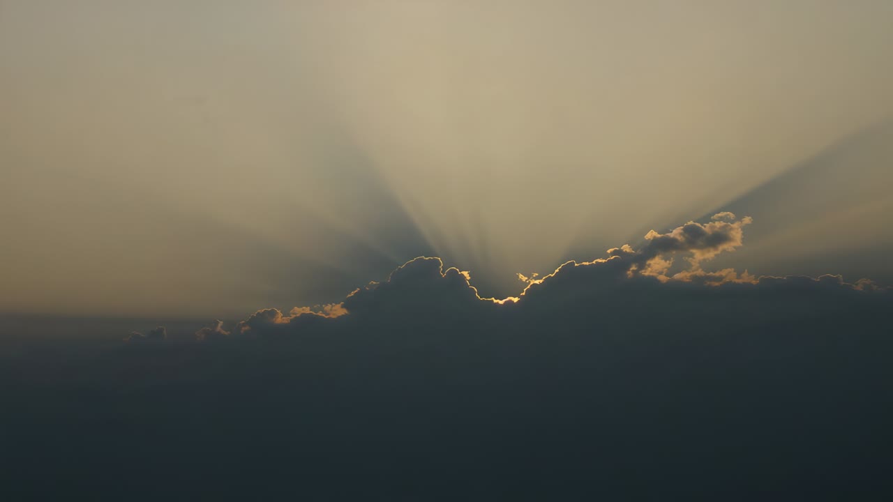 Disco solare in movimento che emerge attraverso una fitta apertura tra le nuvole all'alba, creando raggi di sole e lens flare