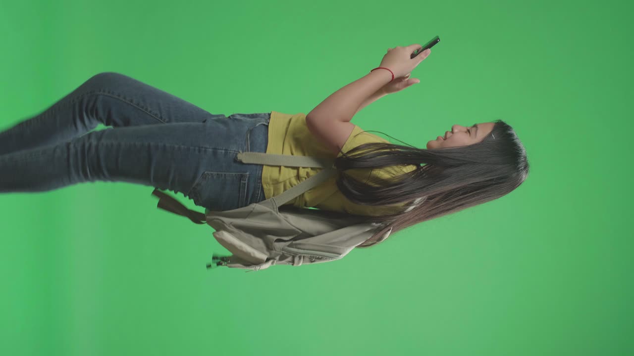 vista lateral de una estudiante asiática que usa un teléfono móvil y camina a la escuela en una pantalla verde
