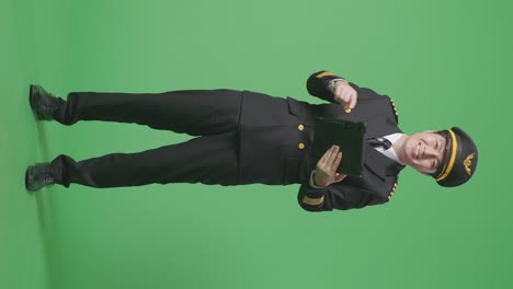 녹색 스크린 배경 스튜디오에 서 있는 동안 손에 태블릿을 가리키며 미소 짓는 아시아 남성 조종사의 몸이 가득 차 있습니다.