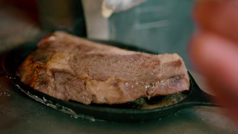 Close-up-view-of-steak-on-the-cast-iron-skillet-over-high-heat-adding-butter-to-the-steak