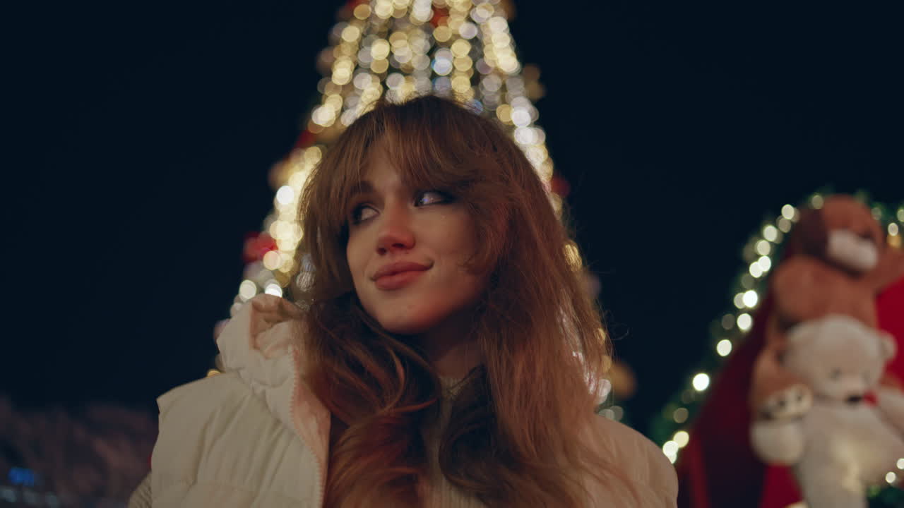 밤 거리에서 크리스마스 조명 장식으로 포즈를 취하는 소녀. 행복한 여성