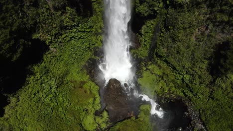 aerial dolly out of salto el leon waterfall falling into rocky natural pool surrounded by green dense woods, pucon, chile