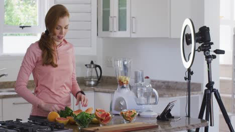 woman chopping fruit and recording it with digital camera in the kitchen