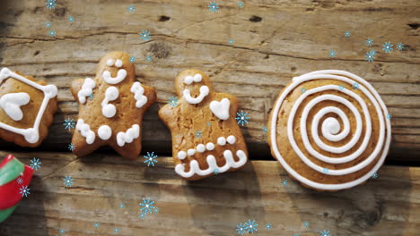 snowflakes falling against gingerbread man cookies and candy cane on wooden surface