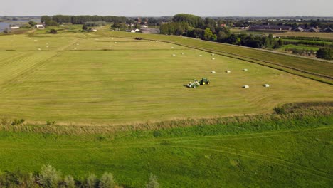 aerial orbiting around a modern tractor producing hay bales on a big farmland