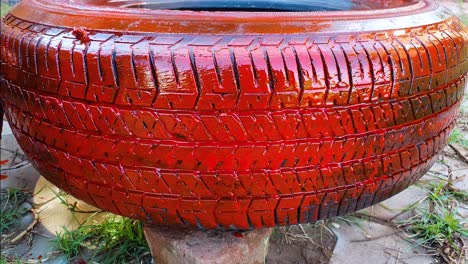 applying red paint on old abandoned car tire for using it as planter