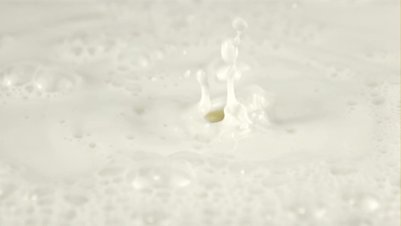 Gocce di latte che schizzano su una superficie liquida bianca al rallentatore