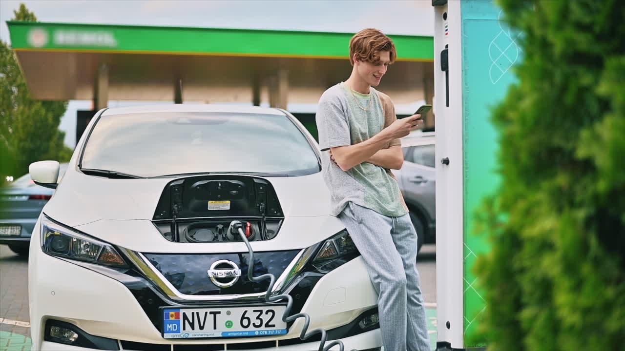 モルドバのキシナウにある充電ステーションで、若い男性が電気自動車に充電器を挿し込んでいる様子。