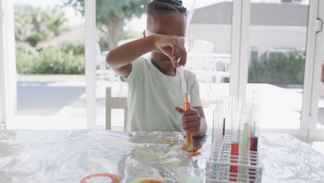 African-american-boy-sitting-at-table-holding-test-tubes-with-liquid,-in-slow-motion