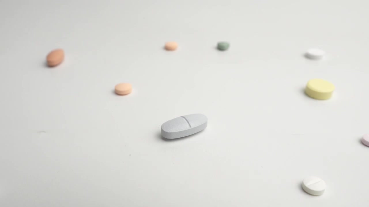 Pillole medicinali colorate assortite sparse su una superficie bianca pulita, carrellata indietro media per rivelare la miscela.