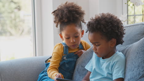 boy and girl playing handheld computer game sitting on sofa at home together