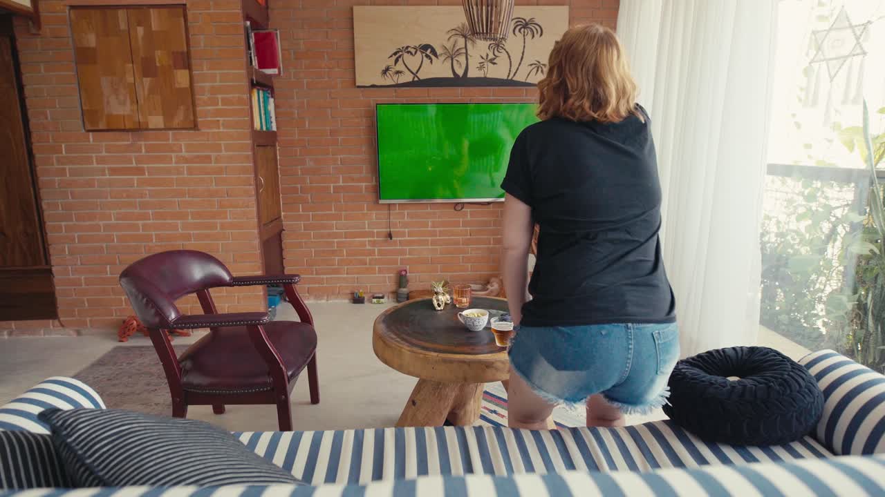 흥분 된 여자 는 아파트, 녹색 스크린 에서 tv 에서 스포츠 를 시청 할 때 점프