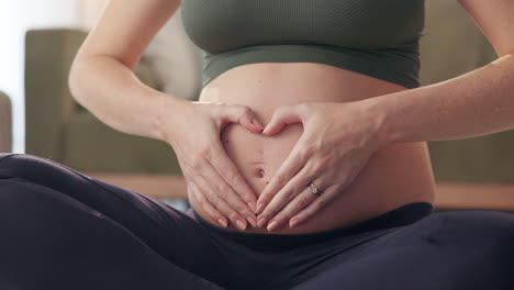 pregnant woman making heart shape with hands on belly