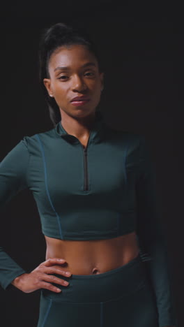 vertical video portrait of serious female athlete wearing tracksuit walking towards camera and into focus training for sports event against black studio background