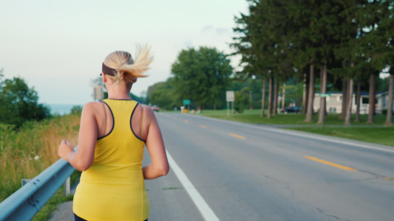 젊은 여성이 전형적인 미국 교외 스테디캠 팔로우 샷을 따라 조깅합니다.