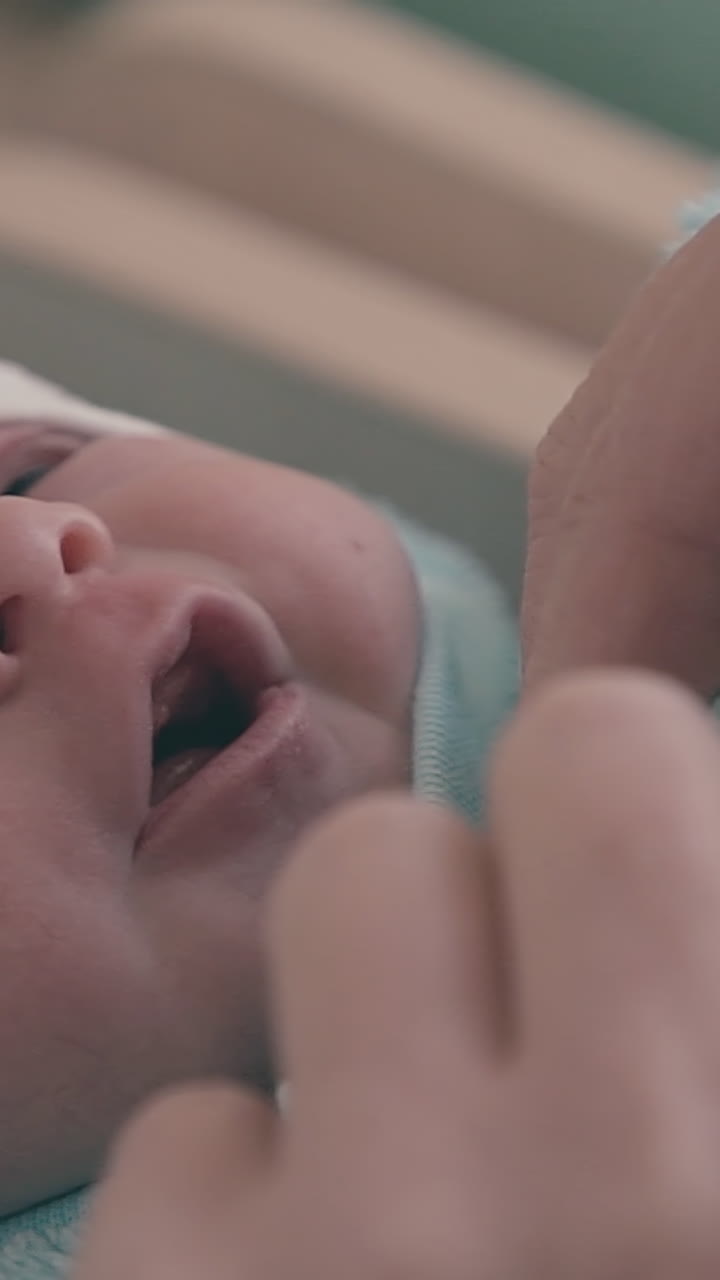 careful young mother puts on cute newborn baby fluffy blue bodysuit over tuxedo extreme close view