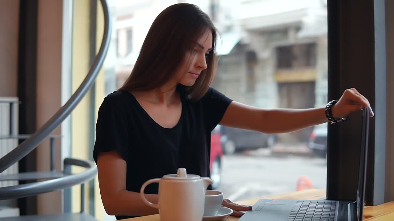 Young woman sitting in the coffee shot having a coffee break, she is opening her laptop and starts working and surfing in the