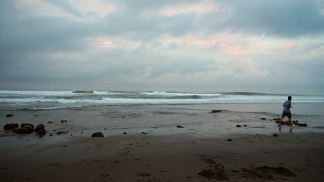 a young man jogs along the sandy beach at sunrise for exercise, captured at echo beach in bali. the scene features soft morning light, gentle waves, and a peaceful coastal setting