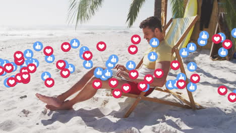 animation of red heart love and like digital icons over man in deckchair with laptop on beach