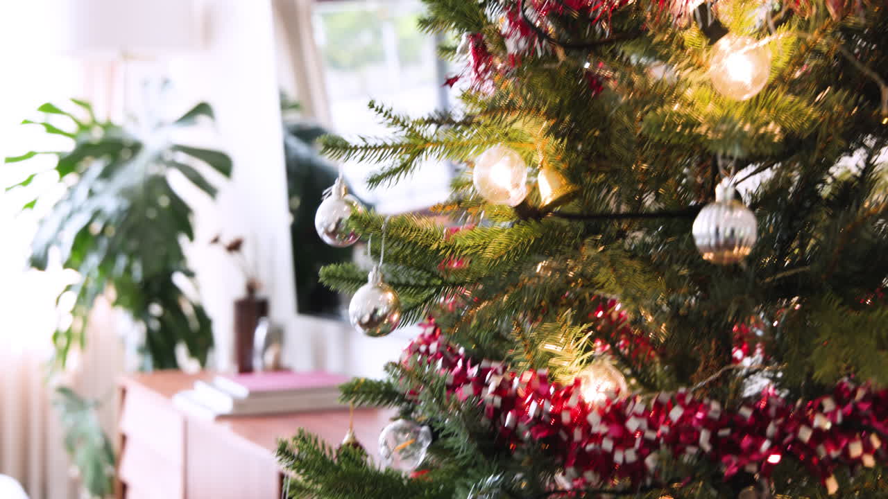 Decorating Christmas tree with colorful ornaments and twinkling lights at home