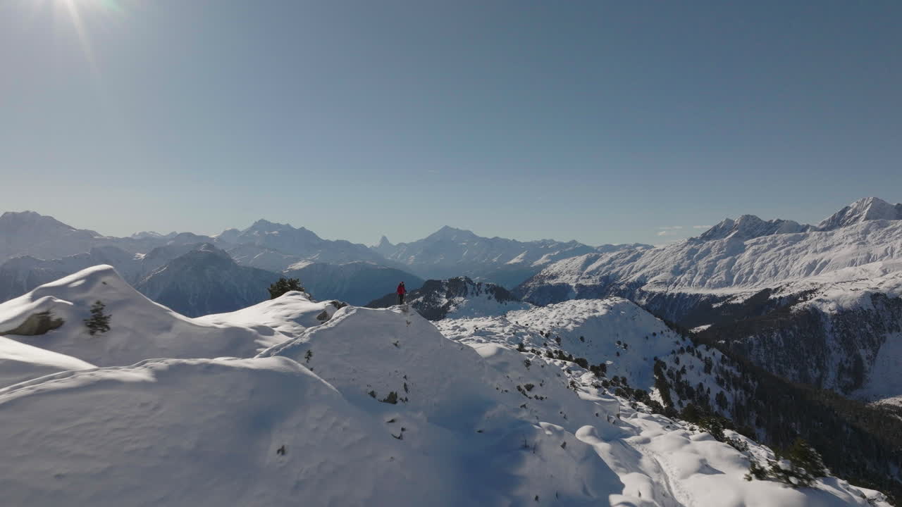 toma aérea en suiza con una persona caminando con raquetas de nieve en un día soleado con un glaciar detrás