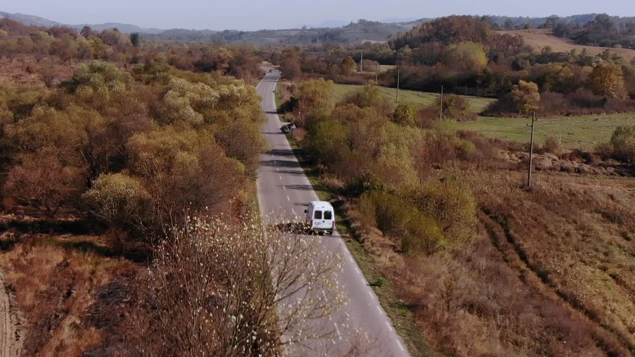 Furgone bianco che percorre una lunga e tortuosa strada di campagna in autunno - vista aerea