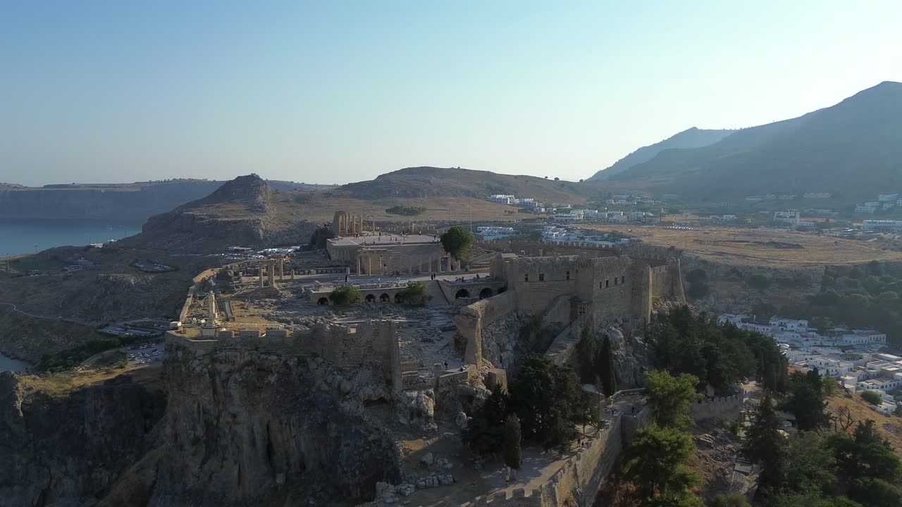 Ripresa cinematografica con drone in allontanamento che rivela l'antica Acropoli di Lindos a Rodi, Grecia. Vista dall'alto del Tempio di Atena, delle mura medievali e del mare. Ideale per film storici e di viaggio.