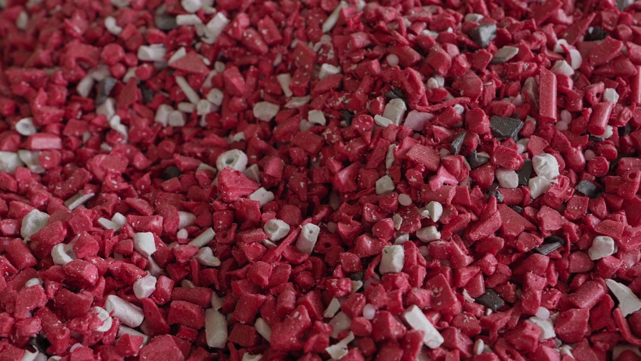 Dense pile of shredded red and white mixed plastic flakes and chips after shredding process