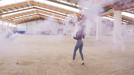 female dancer in an empty warehouse holding smoke grenade