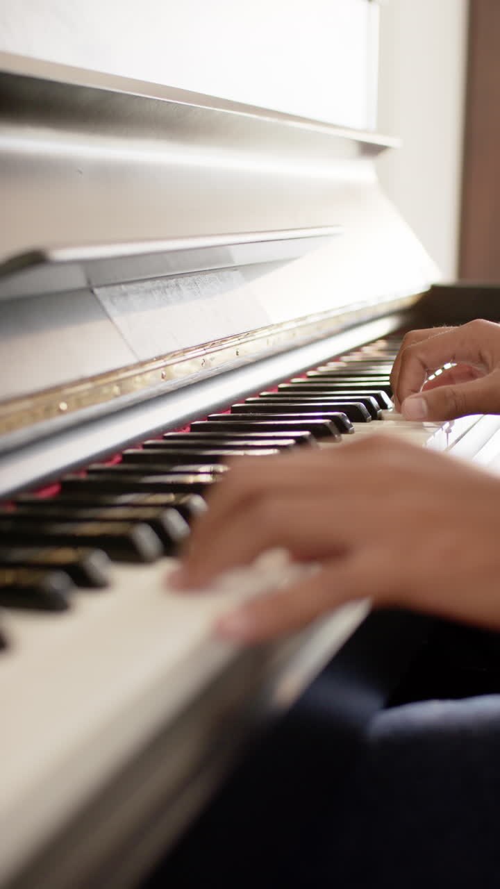 Pystyvideo lähikuvasta anglointialaisen miehen käsistä soittamassa pianoa kotona, hidastettuna.