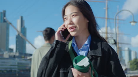 young asian businesswoman walking with coffee outdoors and talking on phone