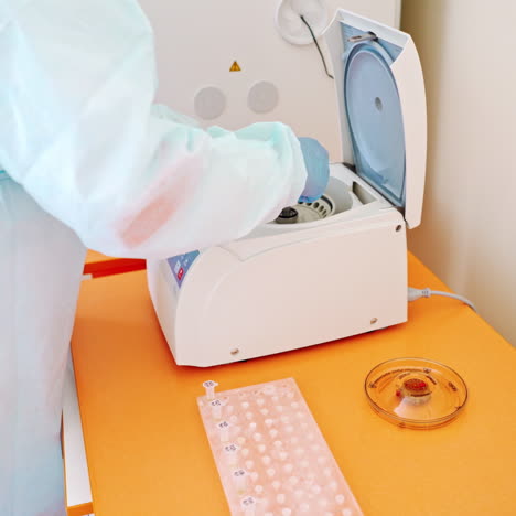 laboratory assistant near automated device for making analysis. female worker in protective uniform takes out test tubes from centrifuge in lab.