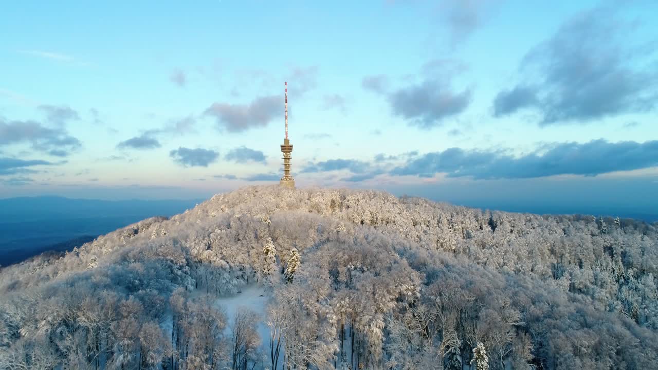 vista aérea de la torre de televisión en la cima de la montaña rodeada de bosque cubierto de nieve al atardecer