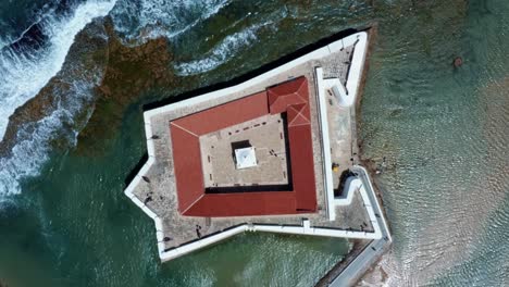 rising bird's eye top aerial drone wide shot of the historic star shaped reis magos fort with waves crashing into the white walls in the beach capital city of natal in rio grande do norte, brazil