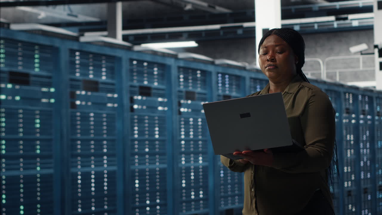Smiling engineer walking in data center with laptop, checking hardware