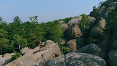 woman jumps touches her knees with the palms of her hands. beautiful lady doing workout on rock