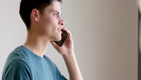 Focused-biracial-man-talking-on-smartphone-standing-in-living-room,-slow-motion