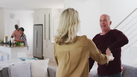 caucasian senior couple dancing in a living room with senior african american couple in background