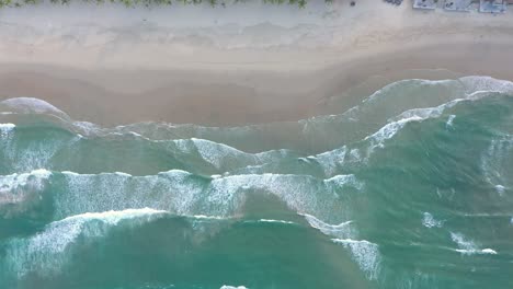 ocean waves crashing into white sand beach filmed from above by drone